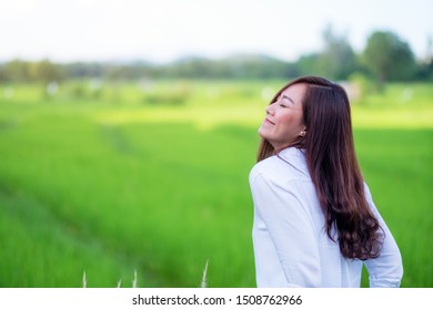 A beautiful asian woman standing in front of a green rice field with feeling relaxed and happy