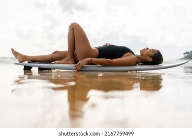 Beautiful Asian Woman Surfer In Swimwear Relaxing On Surfboard After Surfing At Tropical Beach At Summer Sunset. Wellness Female Enjoy Outdoor Lifestyle Water Sport Surfing On Holiday Travel Vacation