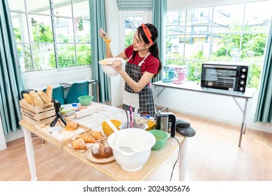 Beautiful Asian Woman Teaching How To Make Bread Bakery And Using The Camera To Record Live Online Social Media Vlogger Or Small Business Blogger Live Streaming Online, Live, Zoom.