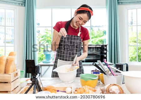 Beautiful Asian woman teaching how to make bread bakery and using the camera to record live online social media Vlogger or small business blogger live streaming online, live, zoom.