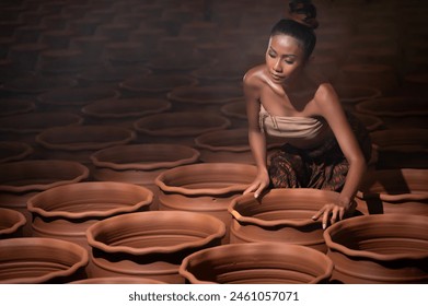 Beautiful Asian woman in traditional Thai dress potter examining pottery in studio - Powered by Shutterstock