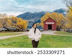 Beautiful asian woman traveling in Glenorchy with red boatshed by Lake Wakatipu on autumn at South Island of Otago, New Zealand