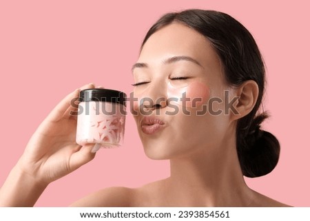 Beautiful Asian woman with under-eye patches and cream on pink background, closeup