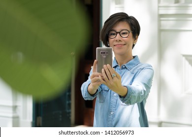 A beautiful asian woman use her smartphone to take a selfie picture, Video call by using FaceTime, Face ID recognition technology, Taking picture, Long-sightedness, social distancing concept.