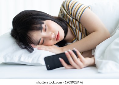 Beautiful Asian Woman Using Phone On Bed In Bedroom
