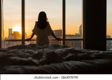 Beautiful asian woman is waking up in the morning, Sun shines on her from the big window. Happy young girl greets new day with warm sunlight flare and city scenery in the window. Co - Shutterstock ID 1863078790