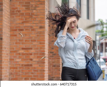 Beautiful Asian Woman Walking On Street Against Strong Wind, With Leaves Fly Around.