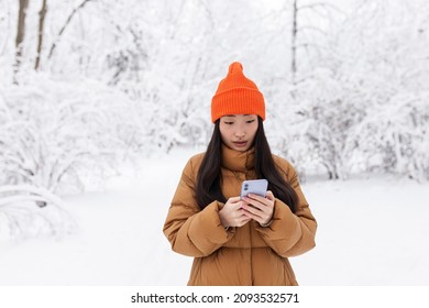 Beautiful Asian Woman Walking In The Park, Uses The Phone For Online Shopping, On A Winter Snowy Day