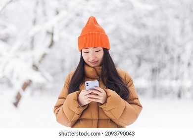 Beautiful Asian Woman Walking In The Park, Uses The Phone For Online Shopping, On A Winter Snowy Day