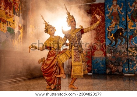 Beautiful Asian woman wear Thai traditional dress action of dancing together with man stand in front of Thai painting on public place wall.