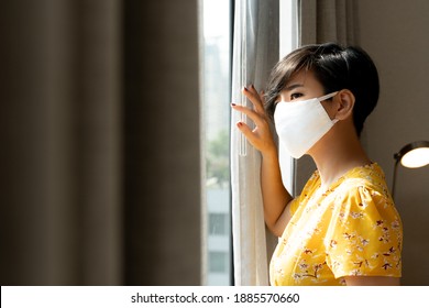 A Beautiful Asian Woman Wearing Cloth Face Mask Stand By The Window In The Room Looking Out Hopefully The Lock Down Will Over Soon. Covid 19 Pandemic Fatique, Stop Asian Hate, Anti-asian Racism.