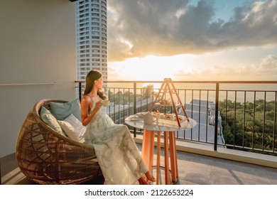 Beautiful asian woman wearing dress enjoying afternoon tea and dessert at balcony on the sunset.
