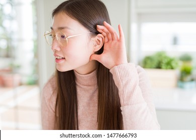 Beautiful Asian Woman Wearing Glasses Smiling With Hand Over Ear Listening An Hearing To Rumor Or Gossip. Deafness Concept.