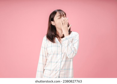 Beautiful Asian woman wearing pajamas bored yawning tired covering mouth with hand. restless and sleepiness.