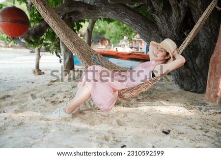 Beautiful Asian woman wearing pink dress and straw hat relaxing on traditional hammock at beach, Koh Samet Thailand.