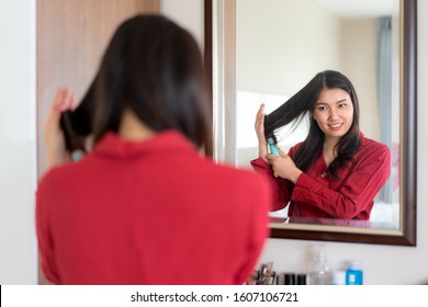 Beautiful Asian Woman Wearing Red Dressed Comb Her Hair And Looking In Mirror In Her Bedroom At Home. Makeup In Morning Getting Ready Before Going To Work.