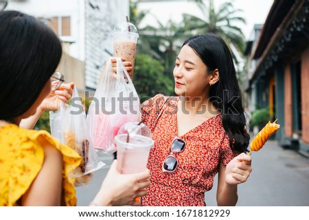 Beautiful asian woman wearing red dress eating street food with friend on yellow dress together on the street - Street food.