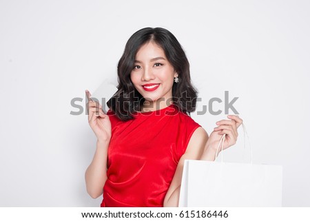Beautiful asian woman wearing a red dress with shopping bag and holding credit card standing over white.