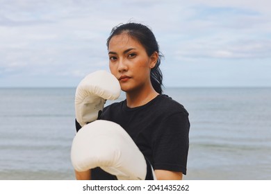 Beautiful Asian woman wearing  white boxing gloves and standing by the sea, Attractive Asian woman boxing on the beach.