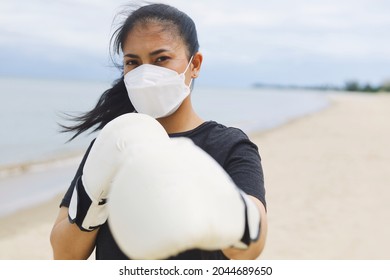 Beautiful Asian woman wearing white boxing gloves surgical mask on the beach,Attractive Asian woman boxing on the beach.