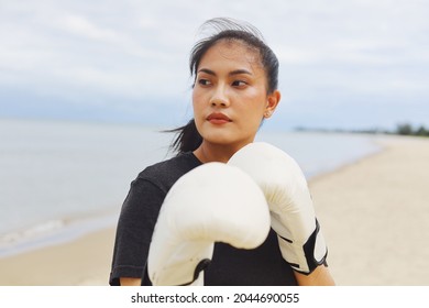 Beautiful Asian woman wearing white boxing gloves and standing by the sea, Attractive Asian woman boxing on the beach.