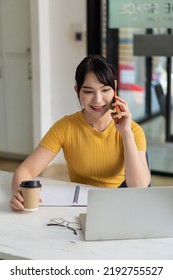 Beautiful Asian Woman Working At Home On Laptop And Talking On Smartphone In Office.