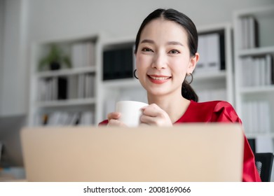 Beautiful Asian Woman Working On A Laptop At Work. She Looked Straight At The Camera And Showed Confidence.