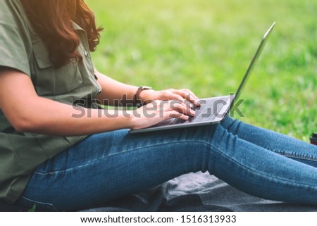 A beautiful asian woman working and typing on laptop keyboard while sitting in the park