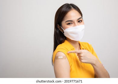 Beautiful asian woman in yellow shirt wearing mask getting a vaccine protection the coronavirus. Happy female pointing arm after receiving vaccination.
