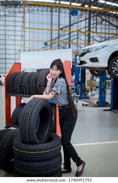 Beautiful Asian women\
stand to introduce new tires and sell tires for safe driving by\
changing new tires. The background is a car repair shop for cars\
that provide service.