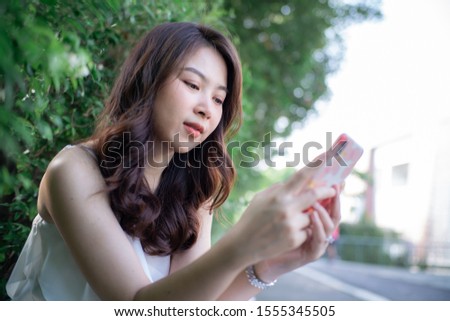 Beautiful asian women use smart phone chat message in city park business technology
