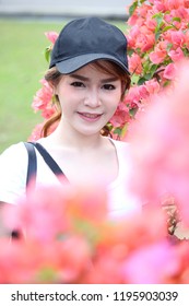Beautiful Asian women Wear a hat and a white shirt are taking photos with pink flowers and holding a mirrorless camera in garden , Location of public park Bangkok, Thailand