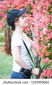 Beautiful Asian women Wear a hat and a white shirt are taking photos with pink flowers and holding a mirrorless camera in garden , Location of public park Bangkok, Thailand