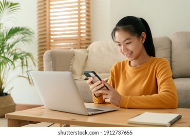 Beautiful Asian Women Wear Long Sleeve Yellow Using Text Message Mobile Phone. Happy Young Woman Using A Phone Smile On The Face While Sitting In Living Room At Home Morning  