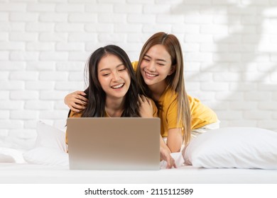 Beautiful Asian Young Lesbian LGBTQ Couple Or Friends Using Computer Laptop Together Smile And Relax On Bed.Happiness LGBTQ Couple Woman Spending Time Together At Home. LGBTQ Pride Month Concept