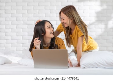 Beautiful Asian Young Lesbian LGBTQ Couple Or Friends Using Computer Laptop Together Smile And Relax On Bed.Happiness LGBTQ Couple Woman Spending Time Together At Home. LGBTQ Pride Month Concept