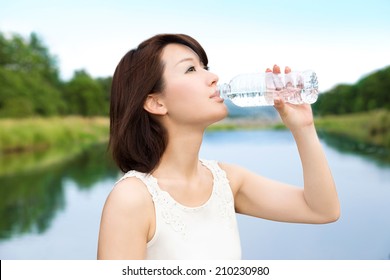 Beautiful Asian Young Woman Drinking A Bottle Of Water In The Nature. 