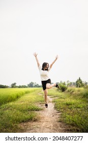 Beautiful Asian Young Woman Enjoy Running And Relaxing At The Rice Field - Meadow. Cheerful Happy Asian Girl Jumping Around The Meadow Or Rice Field In Asia.