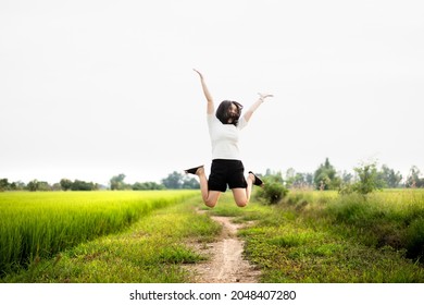 Beautiful Asian Young Woman Enjoy Running And Relaxing At The Rice Field - Meadow. Cheerful Happy Asian Girl Jumping Around The Meadow Or Rice Field In Asia.