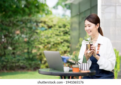 Beautiful Asian Young Woman Greenhouse Worker Selling Small Tree On Social Media Live Stream With Laptop. Landscaping Small Plants And Decorating The Garden In The House. Gardener Working House Plant.