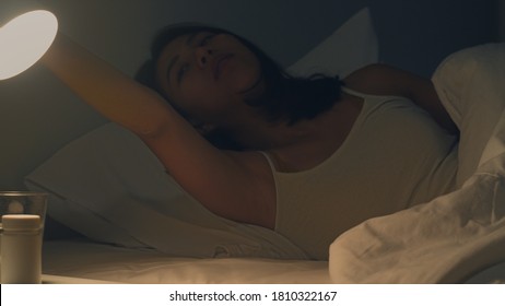 Beautiful Asian Young Woman Sleeping Cozily In Her Bedroom. Indian Female Hand Turning Off On Light Switch Near Bed In Room At Home In Late Night Ready To Sleep. Sweet Dreams And Relaxation Concept.