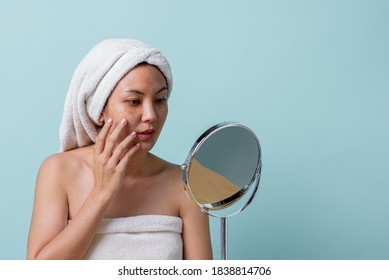 Beautiful Asian young woman touching face and was a feeling of anxiety on her face while looking at the mirror. Skincare and clean concept, Beauty treatment process for rejuvenation.
