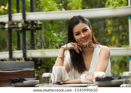 Beautiful Asian Young Woman white short dress sit in Herb garden restaurant empty glass, feel smile and happy lovely time. She wait for boyfriend to have dinner together.