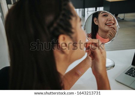 Beautiful asian young woman wrapped in a towel doing her makeup infront of a mirror at the living room. Woman using blush on concept. Beauty concept.