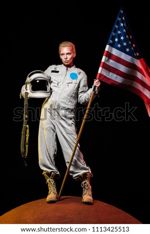 beautiful astronaut in spacesuit holding helmet and american flag on red planet 