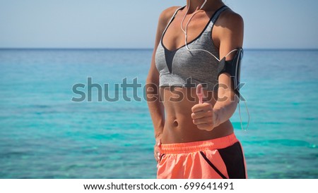 Beautiful athletic body of runner, flat belly in orange shorts white headphones background of blue sea.