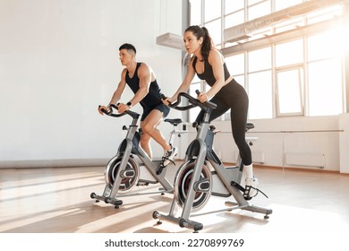 beautiful athletic couple of cyclists train in the fitness room on static bicycle simulator, man trainer and fitness woman go in for sports together on simulators in the morning in bright room - Powered by Shutterstock