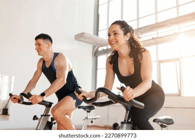 beautiful athletic couple of cyclists train in the fitness room on static bicycle simulator, man trainer and fitness woman go in for sports together on simulators in the morning in bright room - Powered by Shutterstock