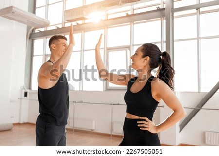 beautiful athletic couple in sportswear greet each other in the gym in the morning, fitness girl and coach man give high five in training in bright room