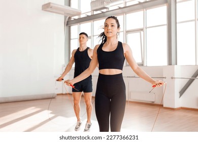 beautiful athletic couple in sportswear jumping rope in the gym in the morning, fitness girl and coach man go in for sports in training in bright room - Powered by Shutterstock